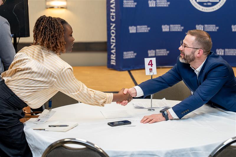 Two people reach out across a table to shake hands.