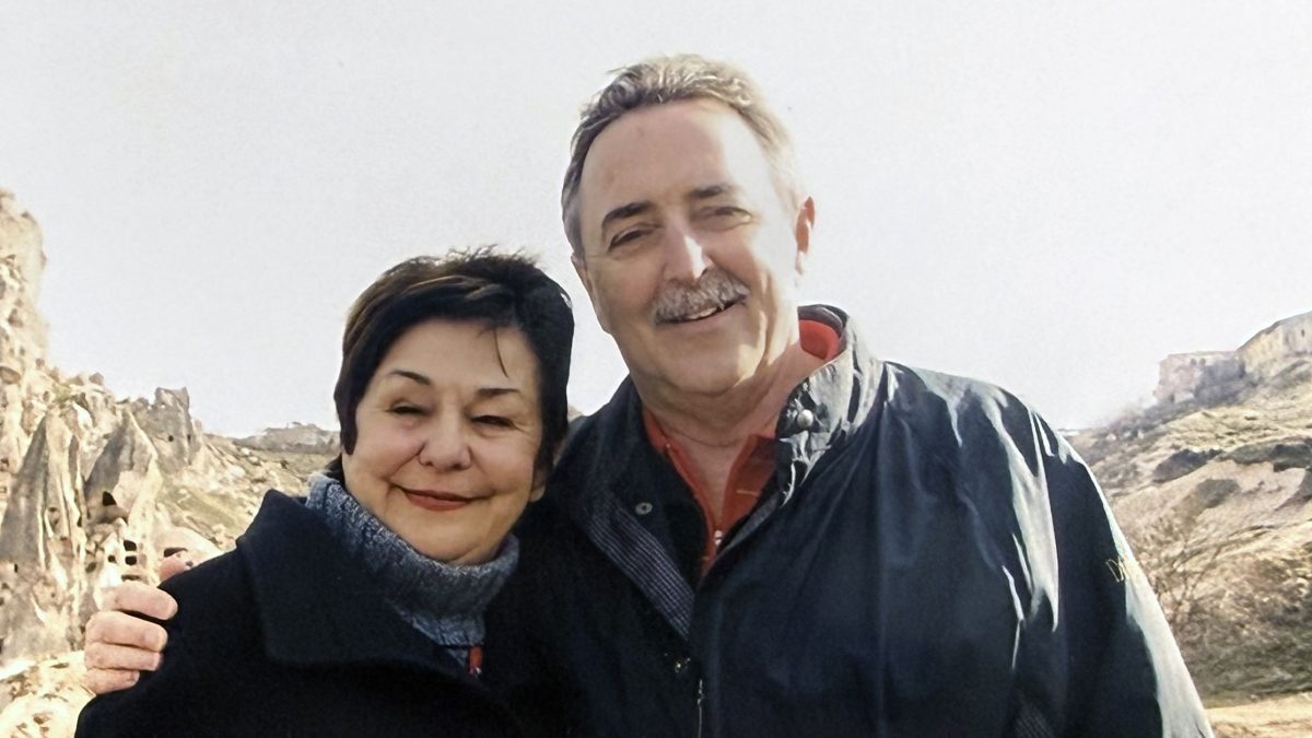 A man poses with an arm around a women's shoulder in front of a rocky background