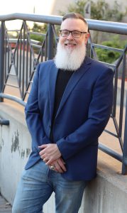 A man smiles while leaning on a railing