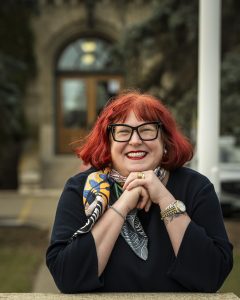 A woman smiles as she leans her elbows on a stone platform. An old building can be seen behind her