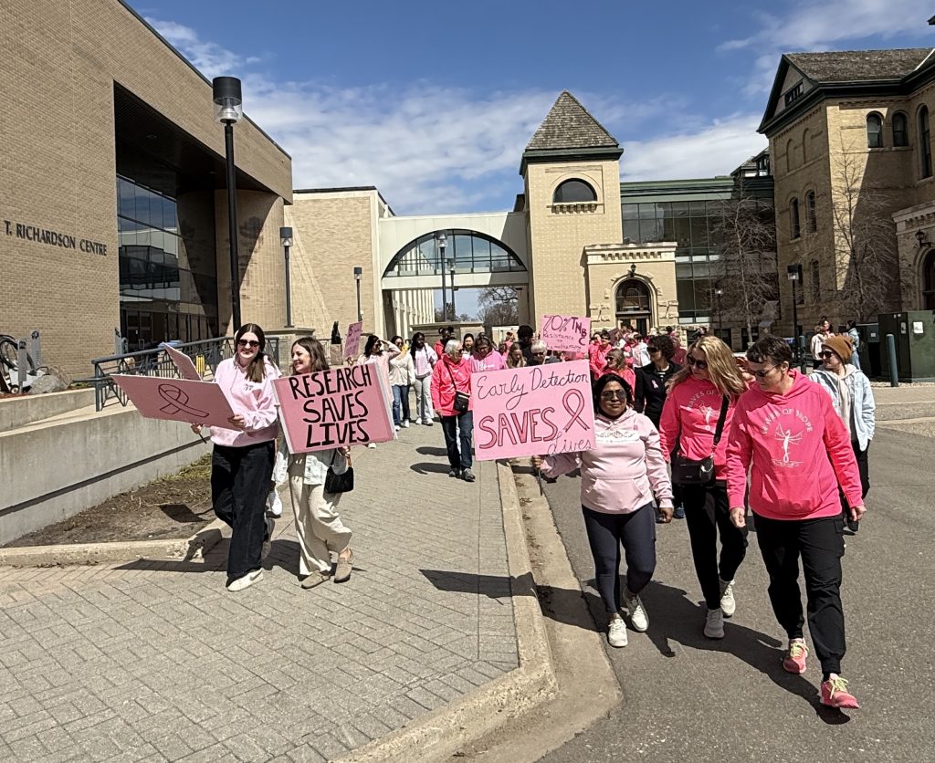 A large group of people walk through a courtyard with signs. One of the signs says "Research Saves Lives" and another one says "Early Detection Saves Lives"