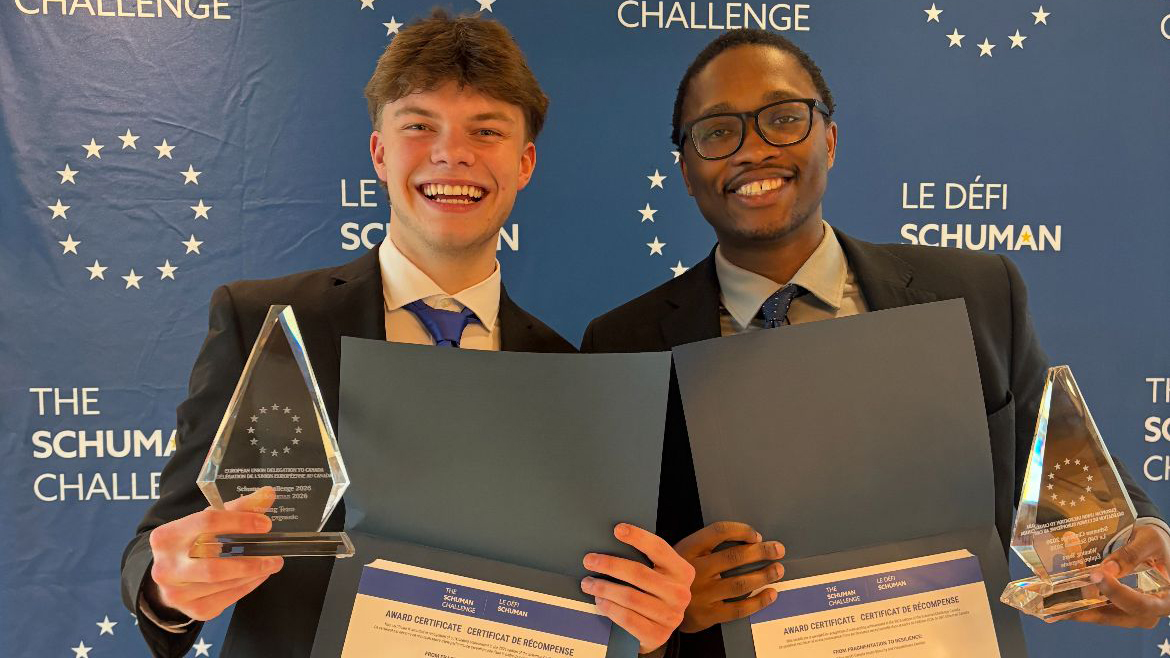 Two men in suits hold trophies and certificates and smile
