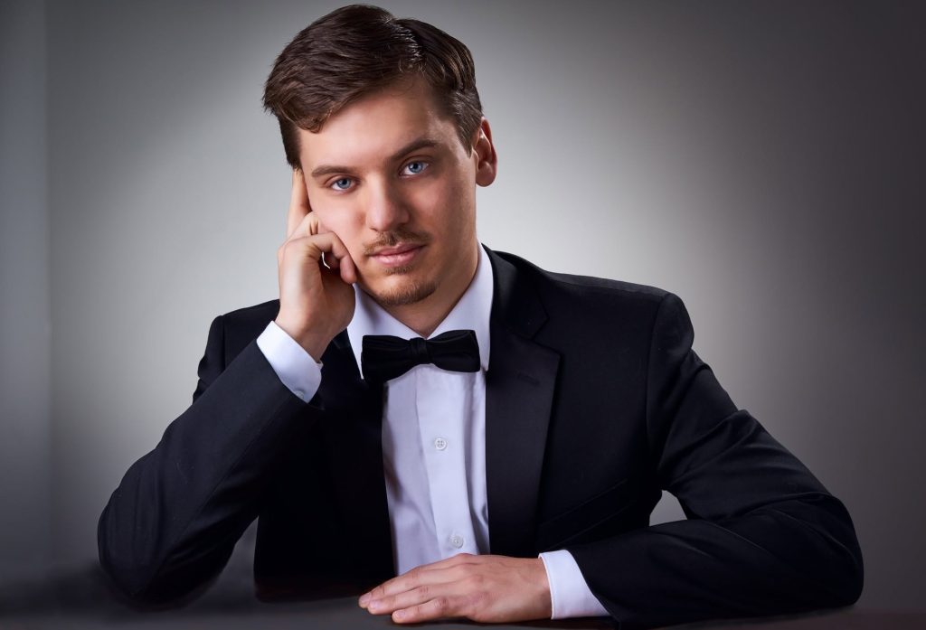 A man in a tuxedo rests on his elbow with his hand against his face