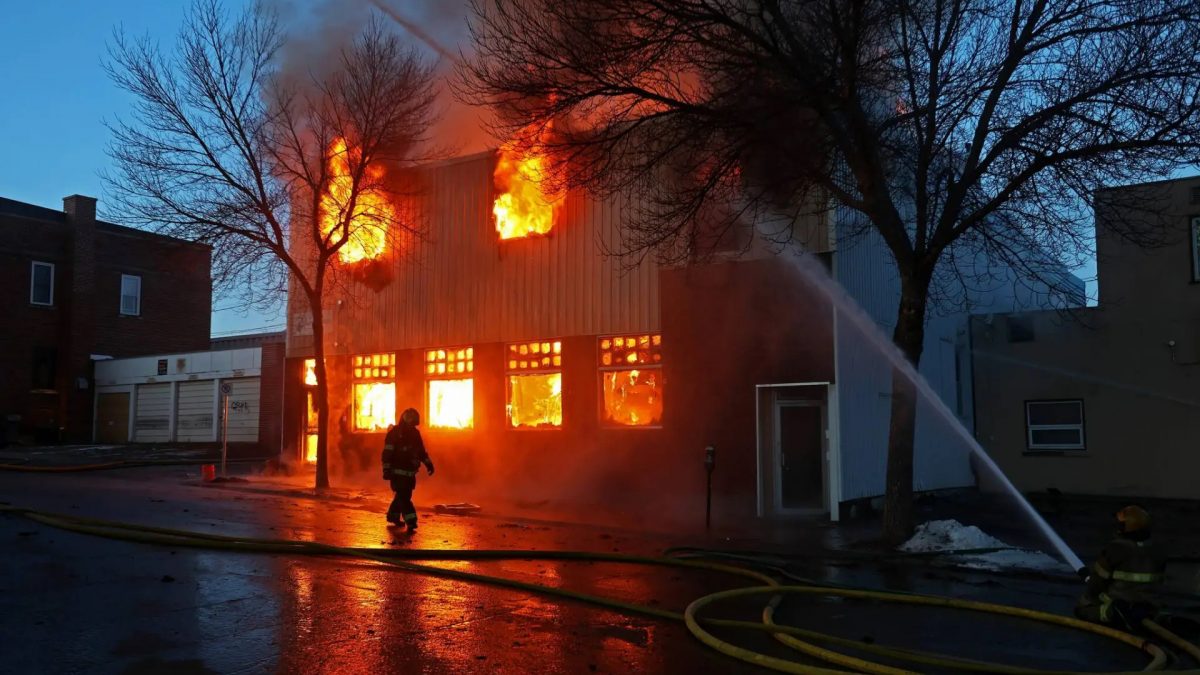 A firefighter is silhouetted against a two-story building engulfed in flames.