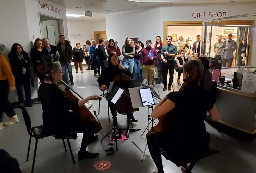 Four cellists perform while surrounded by a large crowd