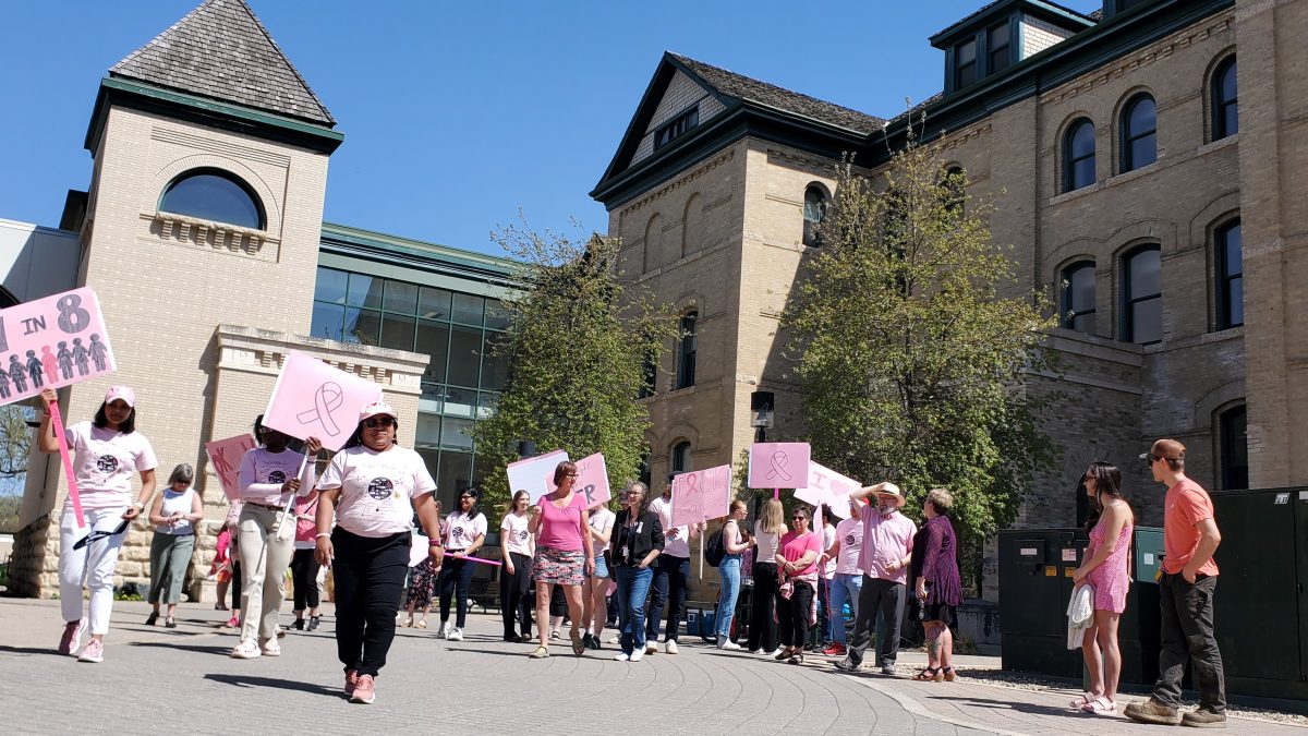 A large group of people, many of them wearing pink, gather in a courtyard between buildings. Many of them are wearing pink.