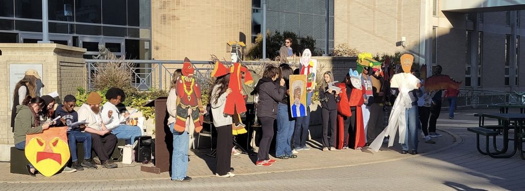 A large group of students line up. Some are holding puppets.