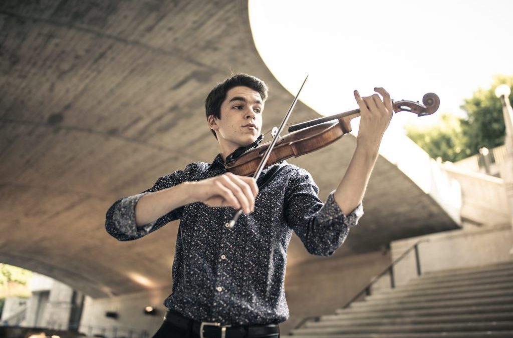 Photo looking up at a man playing violin with stars and a large concrete platform above him