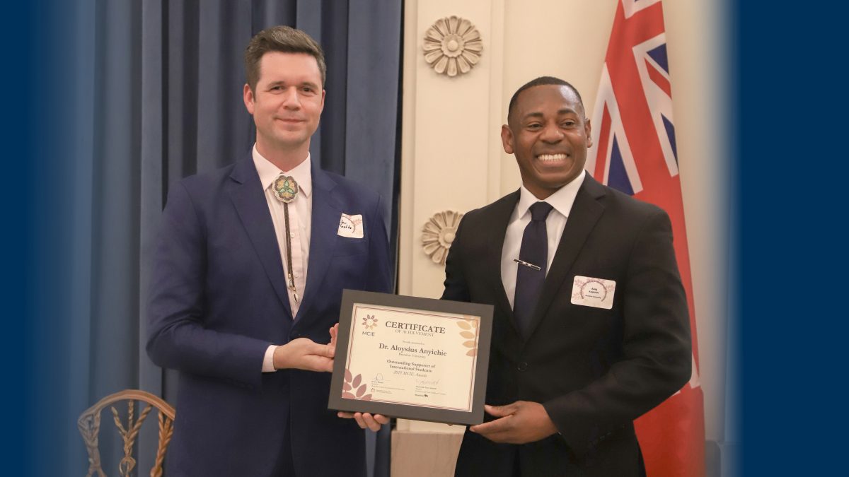 Two men pose with a certificate in a ceremonial space.