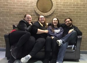 Four students sit on a couch in front of a brick wall.