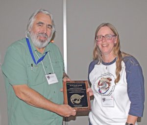 Steve Hecnar and Pamela Rutherford pose, holding a plaque between them