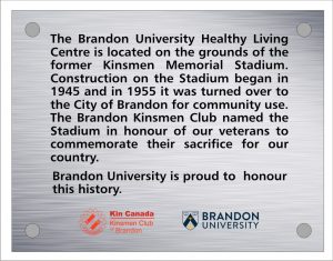 Plaque inscription reads: "The Brandon University Healthy Living Center is located on the grounds of the former Kinsmen Memorial Stadium. Construction on the Stadium began in 1945 and in 1955 it was turned over to the City of Brandon for community use. The Brandon Kinsmen Club named the Stadium in honour of our veterans to commemorate their sacrifice to our country. Brandon University is proud to honour this history.
