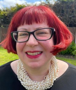 A smiling woman with red hair and distinctive glasses