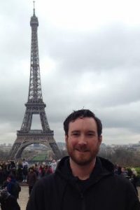 Cameron Watson poses with a picture of the Eiffel Tower in the background