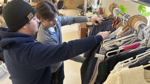 Two young men browse a rack of clothing