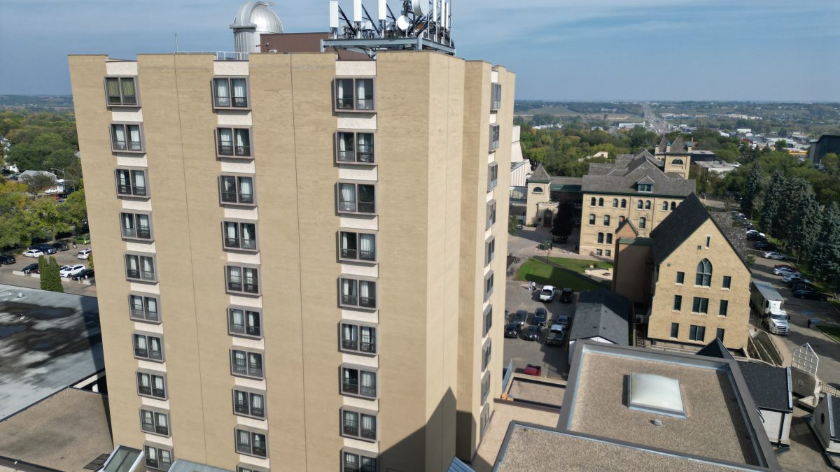 A large residential tower in the foreground, with an observatory and antenna on top, with historic buildings in the background.