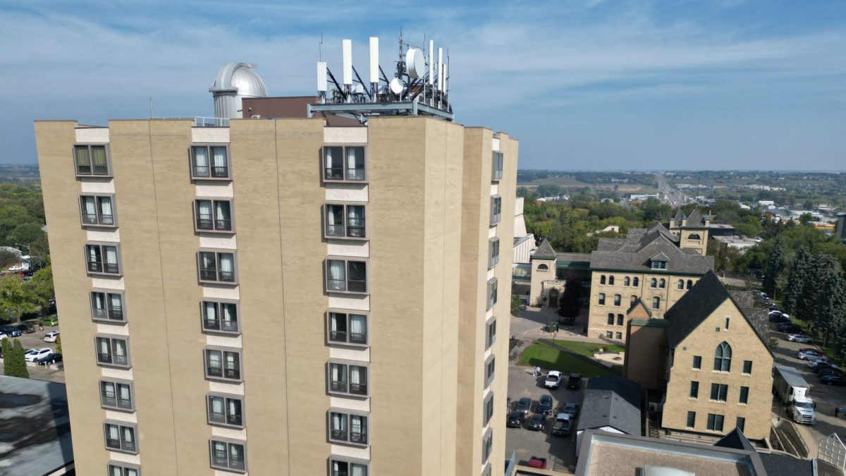 A large residential tower in the foreground, with an observatory and antenna on top, with historic buildings in the background.