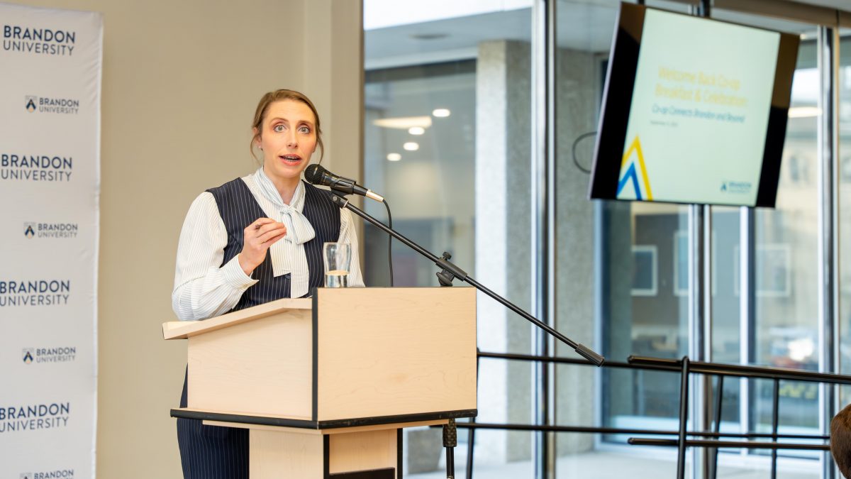 A woman speaks from a podium. A screen behind her says "BU Co-op Welcome Back Breakfast."