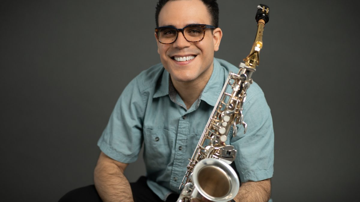 A man smiles while holding a saxophone