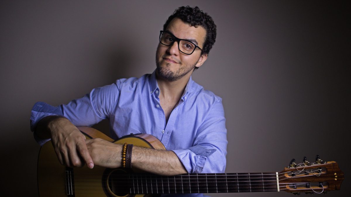 A man smiles while holding a guitar