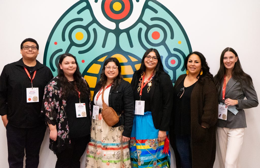 A group of people stand in front of a colourful mural.