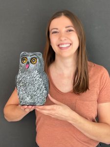 A woman poses with an owl figurine.