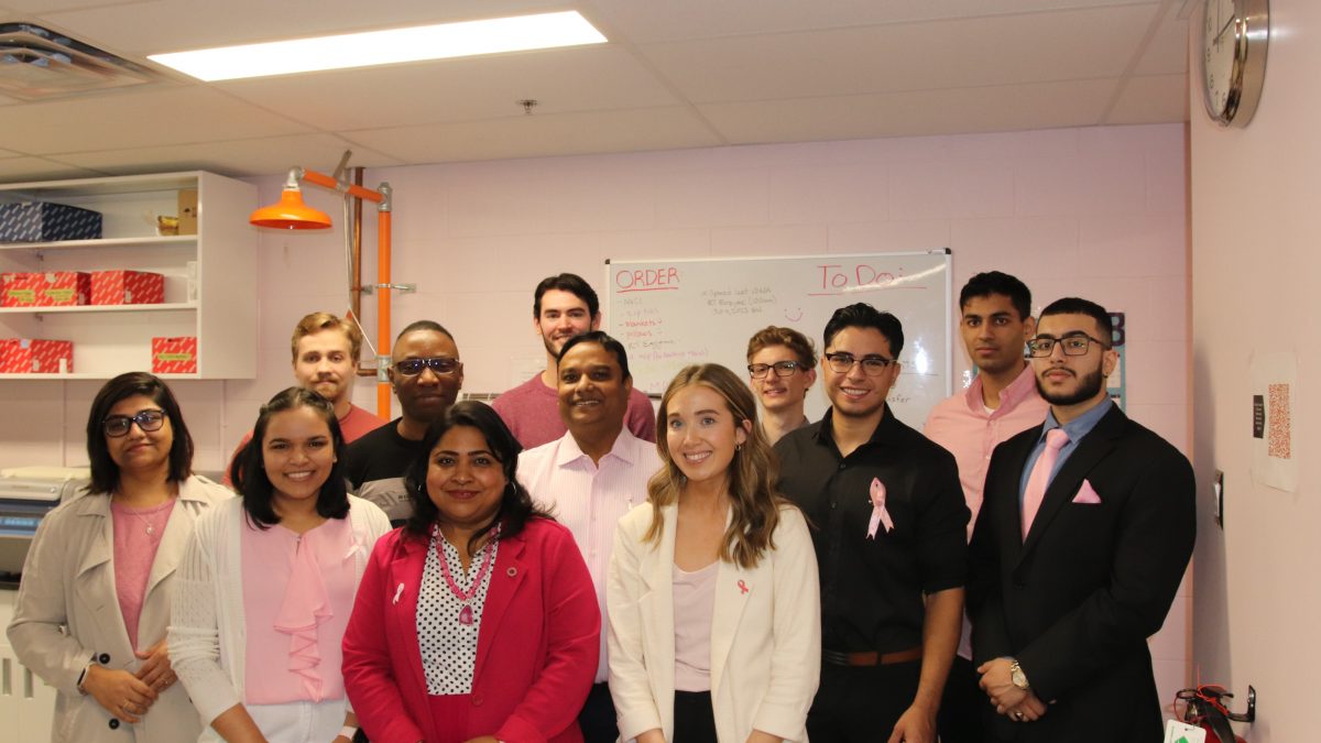 A large group of people pose in a lab. Several of them are wearing pink