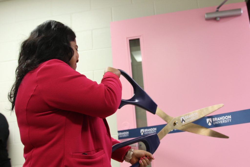 A woman cuts a Brandon University ribbon with a large pair of scissors