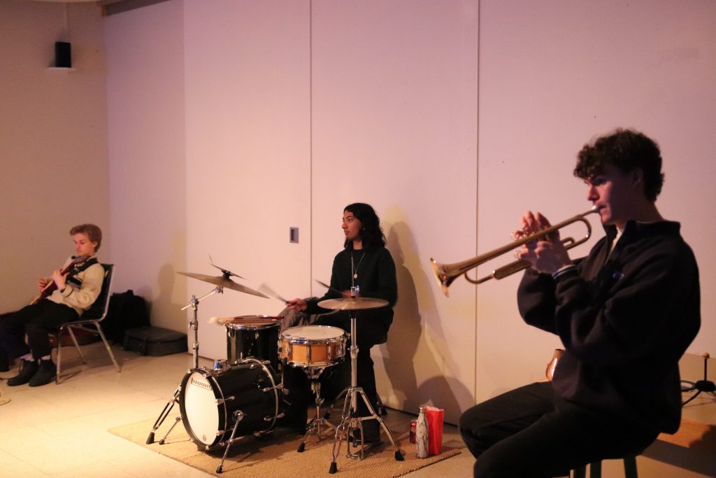 A trumpet player, a drummer and a guitarist sit and play
