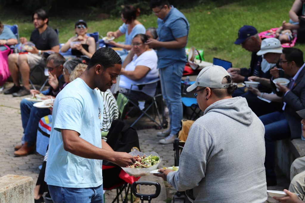 Two men serve salad from a large bowl