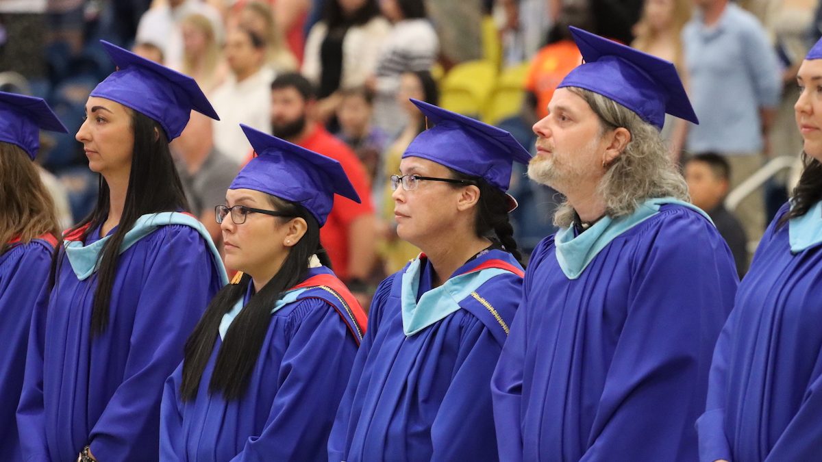 A row of graduates stand side-by-side in their gowns and caps