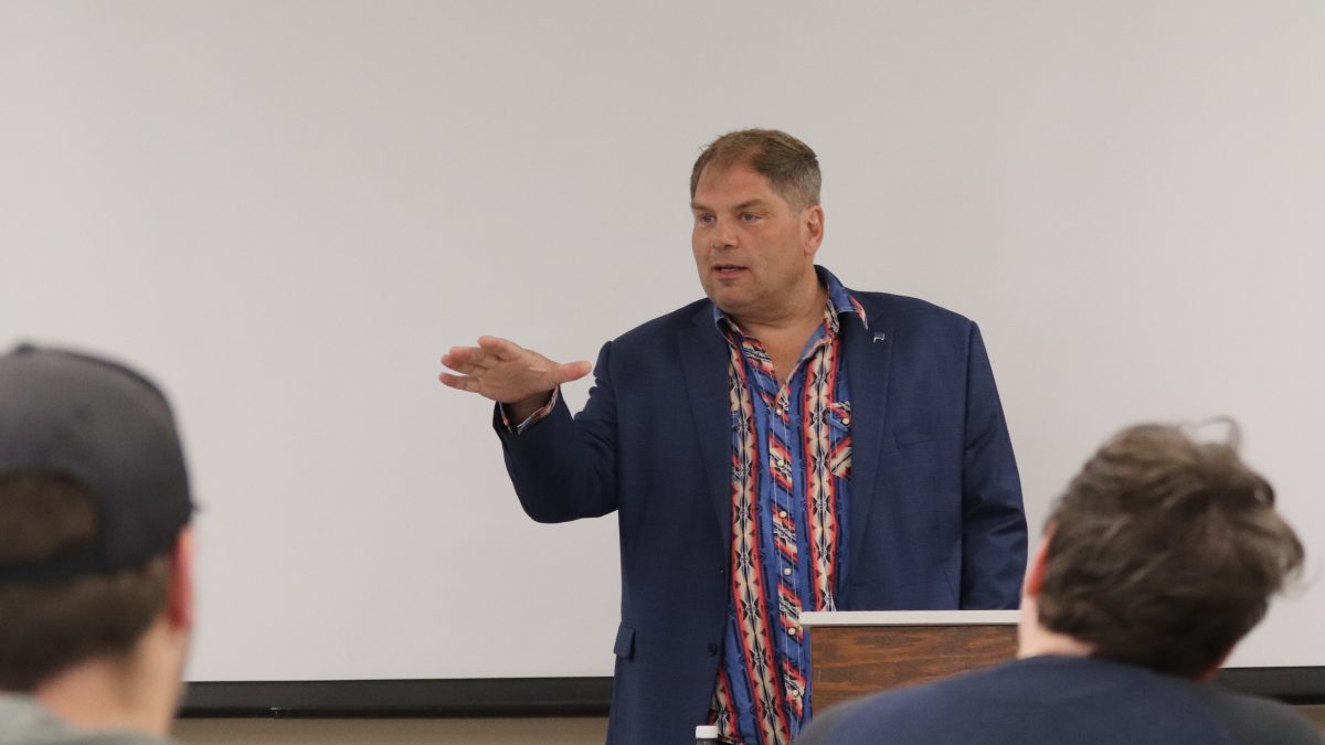 A man motions with his hand while speaking in front of a group