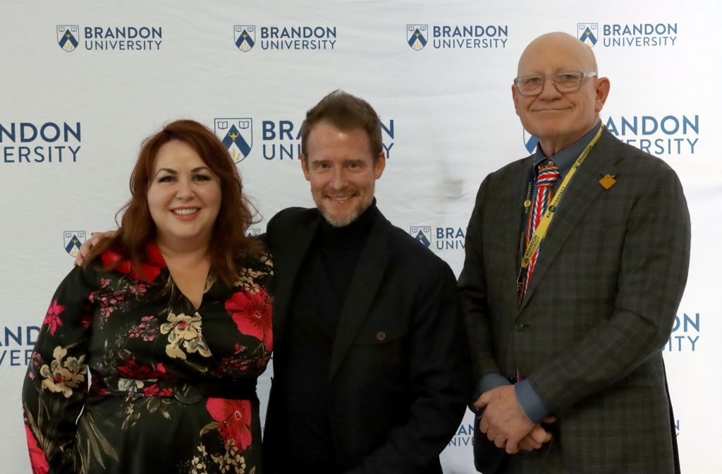 A woman poses next to two men