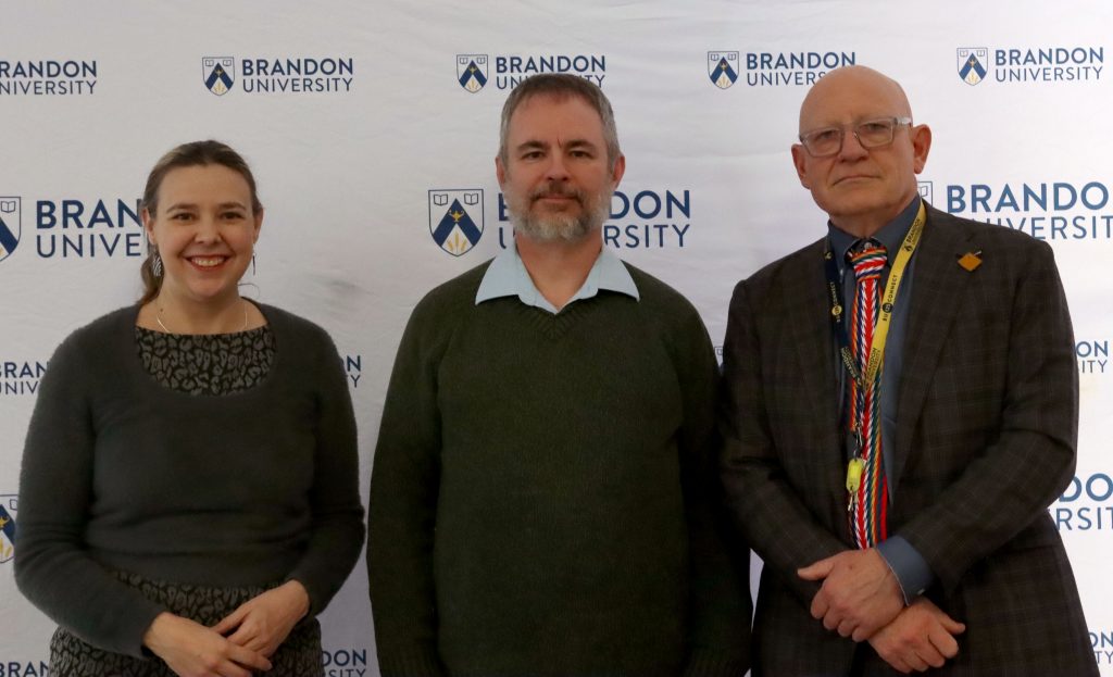 A woman poses next to two men