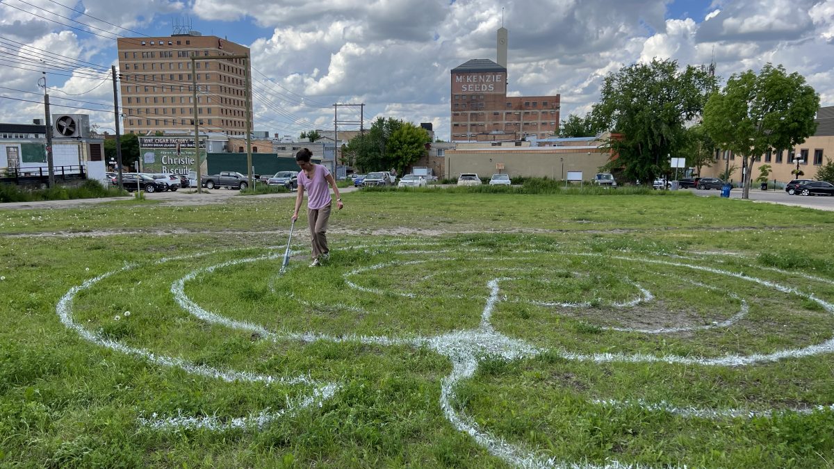 a woman spray paints on the grass of a vacant lot