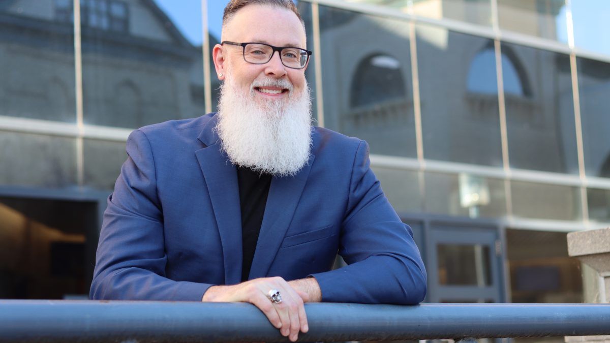 A main leans on a railing in front of reflective windows