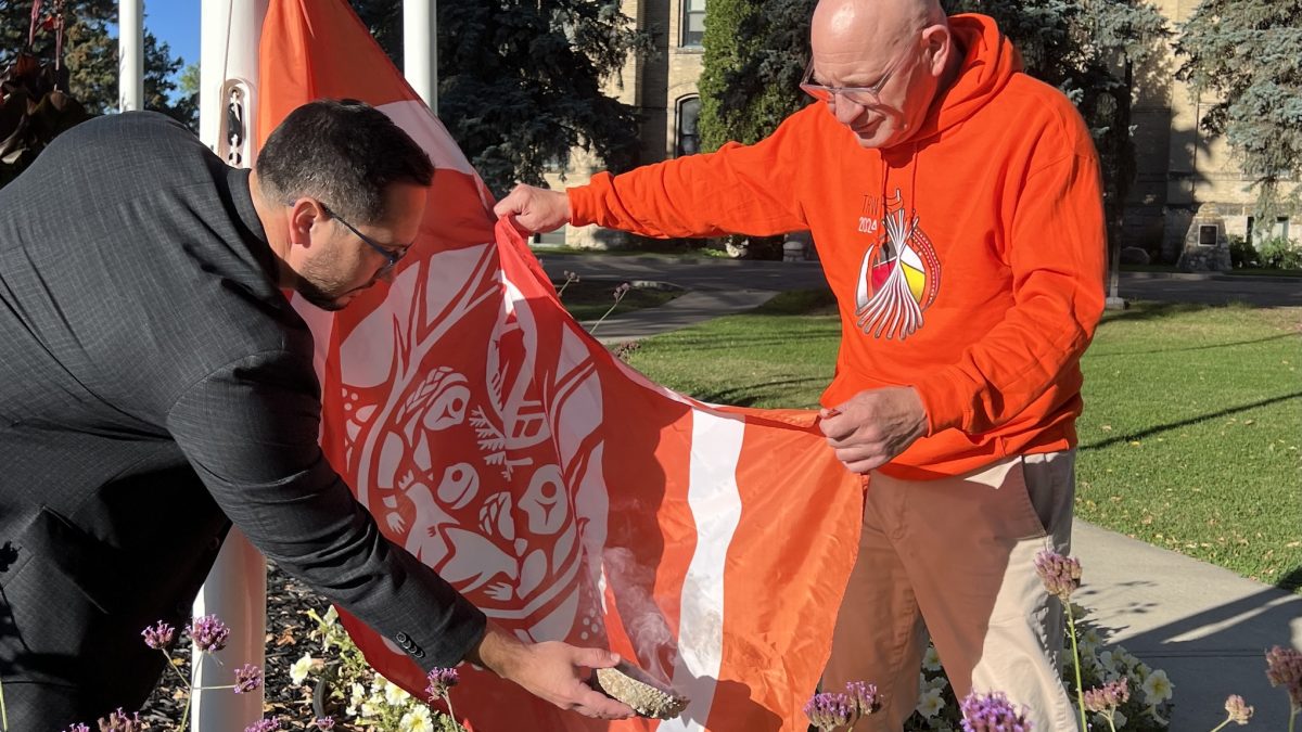 A man reaches out with a bowl toward a flag held by another man