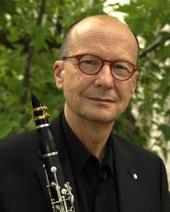 Headshot of a man in front of a tree, holding a clarinet