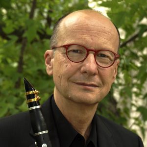 Headshot of James Campbell posing in front of a tree, holding his clarinet