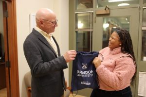 A man and a woman smile at each other while holding a Brandon University bag between them.