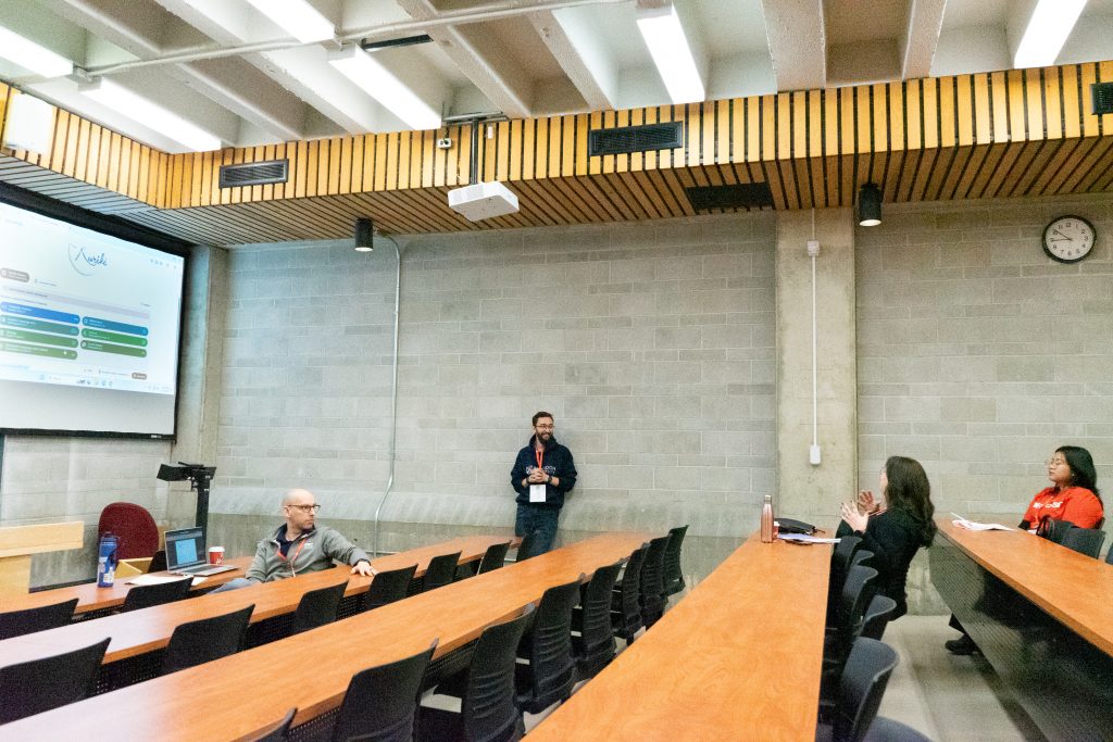 A students stands against a wall in a lecture theatre.