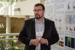 Man with beard and glasses standing in front of an academic poster