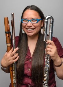 A woman smiles while holding various types of flutes