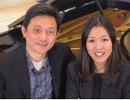 Ning Lu and Jie Lu pose, smiling, in front of a piano