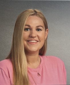 Portrait of a smiling young woman with blond hair in a pink shirt.