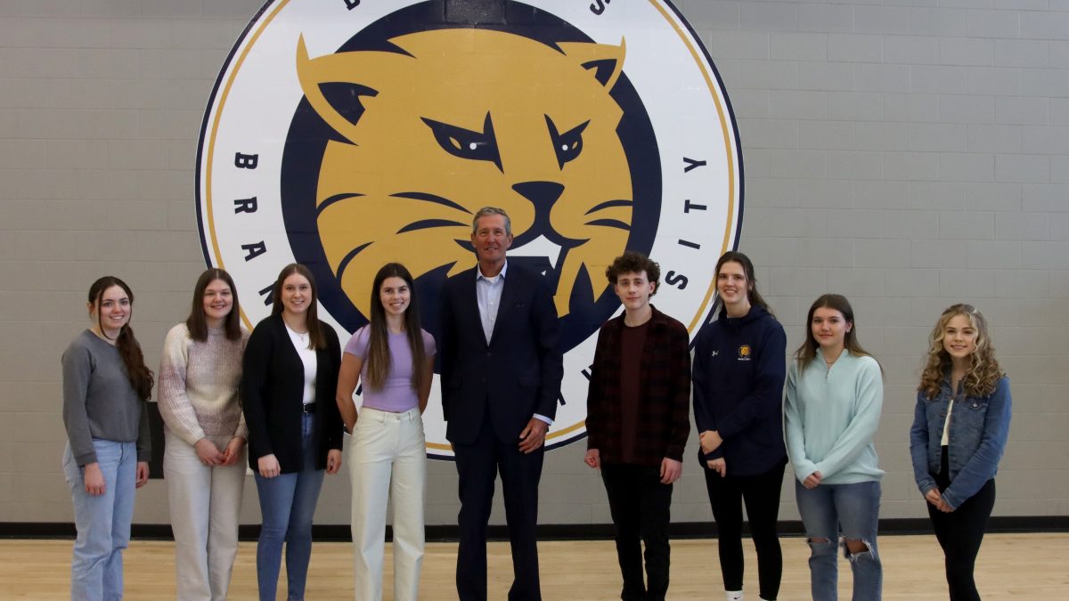A group of students stand with a tall man, in front of a BU Bobcats logo.