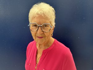 Woman with white hair and glasses in a magenta top