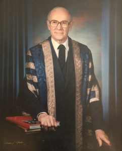 Formal portrait of a man in glasses and academic robes.