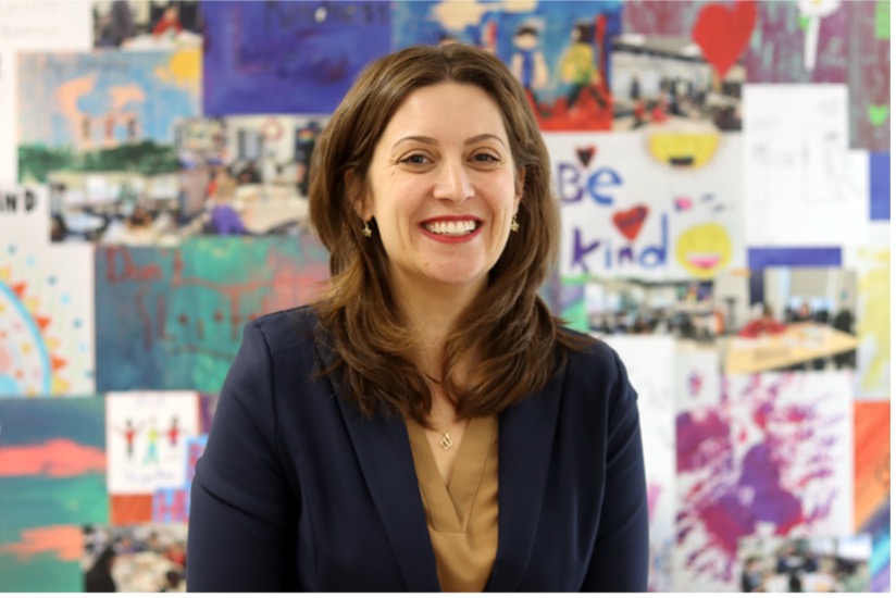 A woman smiles while posed in front of a wall covered with artwork