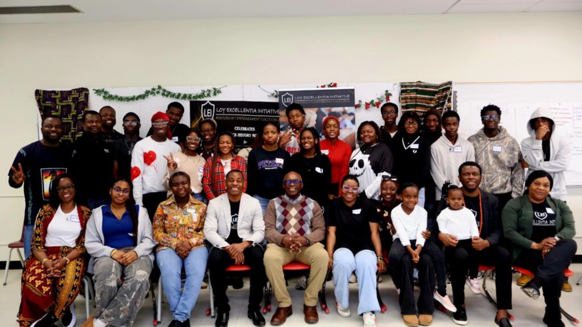 A large group of people pose for a picture. A row of people sit in the front, while others stand in the back
